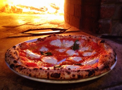 freshly baked margherita pizza in front of a wood fired oven